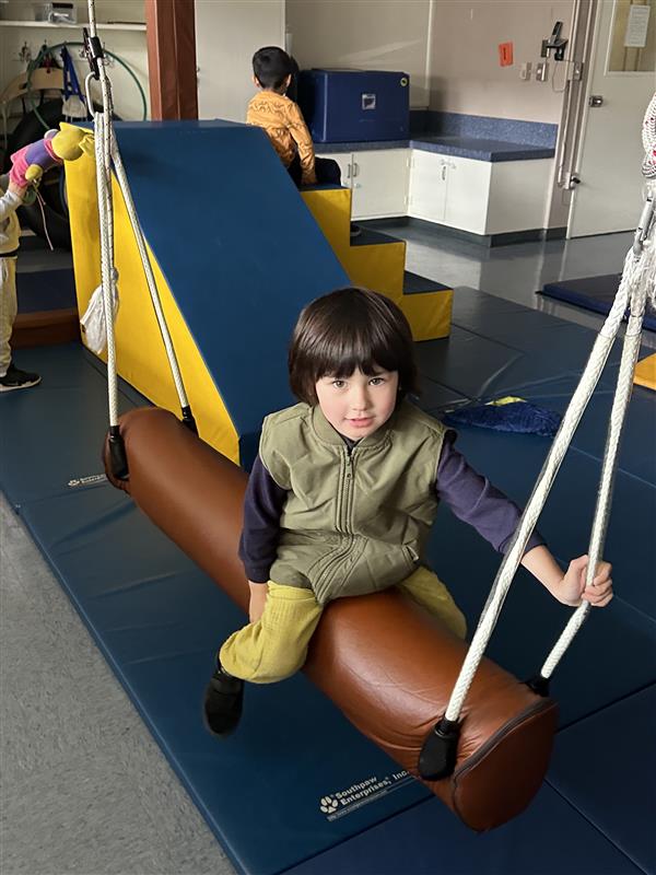 A student sitting on an occupational therapy rocking log looking at the camera. 